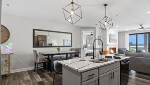 Una cocina moderna con una isla central, luces colgantes y un comedor con un espejo grande.