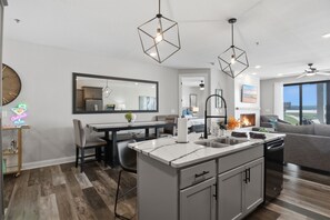 A modern kitchen with a central island, pendant lights, and a dining area with a large mirror.