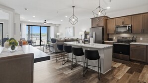 Una cocina moderna con una isla central, taburetes de bar, electrodomésticos de acero inoxidable y vistas al exterior.