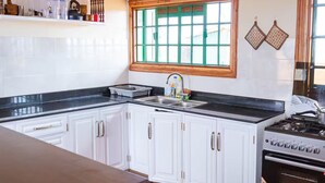 Una cucina con mobili bianchi, un piano di lavoro nero, una finestra con vetri verdi e un fornello.