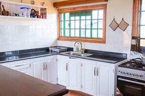 Una cocina con armarios blancos, encimera negra, ventana con vidrios verdes y una estufa.