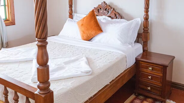 Un letto a baldacchino con struttura in legno, una coperta bianca e un tappeto decorato sul pavimento.
