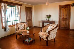 Una habitación con dos sillones tapizados, una mesa de centro de madera, una mesita con un florero y una puerta de madera.