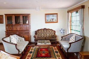 Un salon comprenant un canapé, deux fauteuils, un meuble, un ventilateur et un tapis.