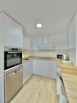 Una cocina moderna con armarios blancos, horno empotrado, microondas y encimera de madera.