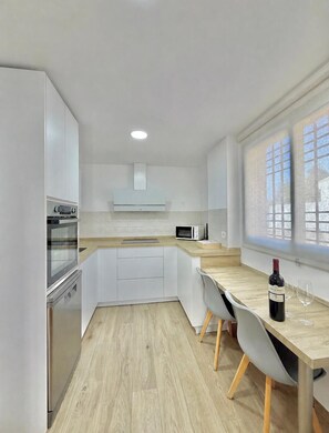 A modern kitchen with white cabinetry, a built-in oven, microwave, and a dining area with a wooden table and chairs.
