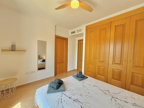 Un dormitorio con cama, ventilador de techo, espejo y armarios de madera.