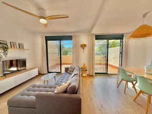 A modern living room with a sofa, TV, dining table, chairs, and a ceiling fan.