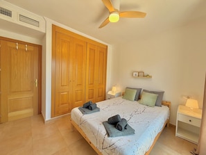 Un dormitorio con una cama, dos mesitas de noche, un ventilador de techo y un armario grande.