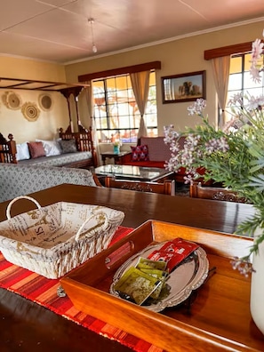 A room with a wooden dining table, a sofa, and a window with curtains.
