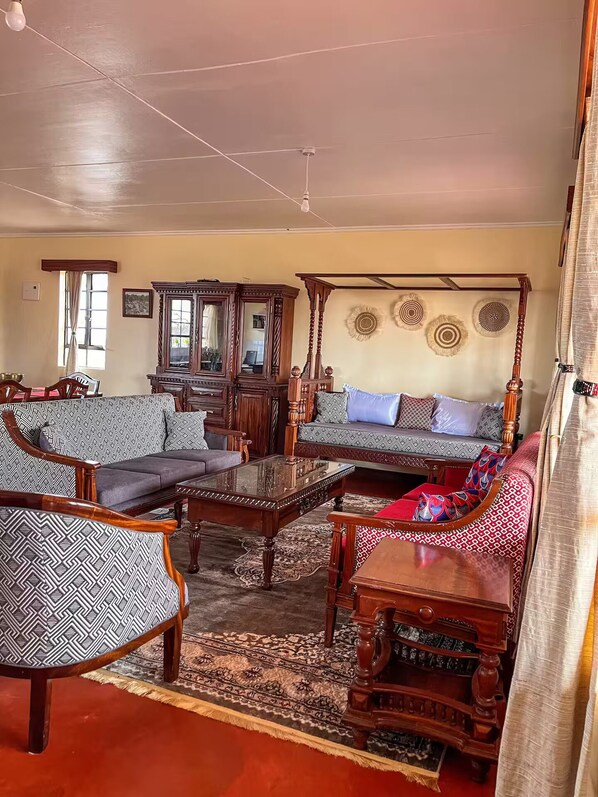 A traditional living room with a sofa, armchairs, a coffee table, a wooden cabinet, and a four-poster bed.