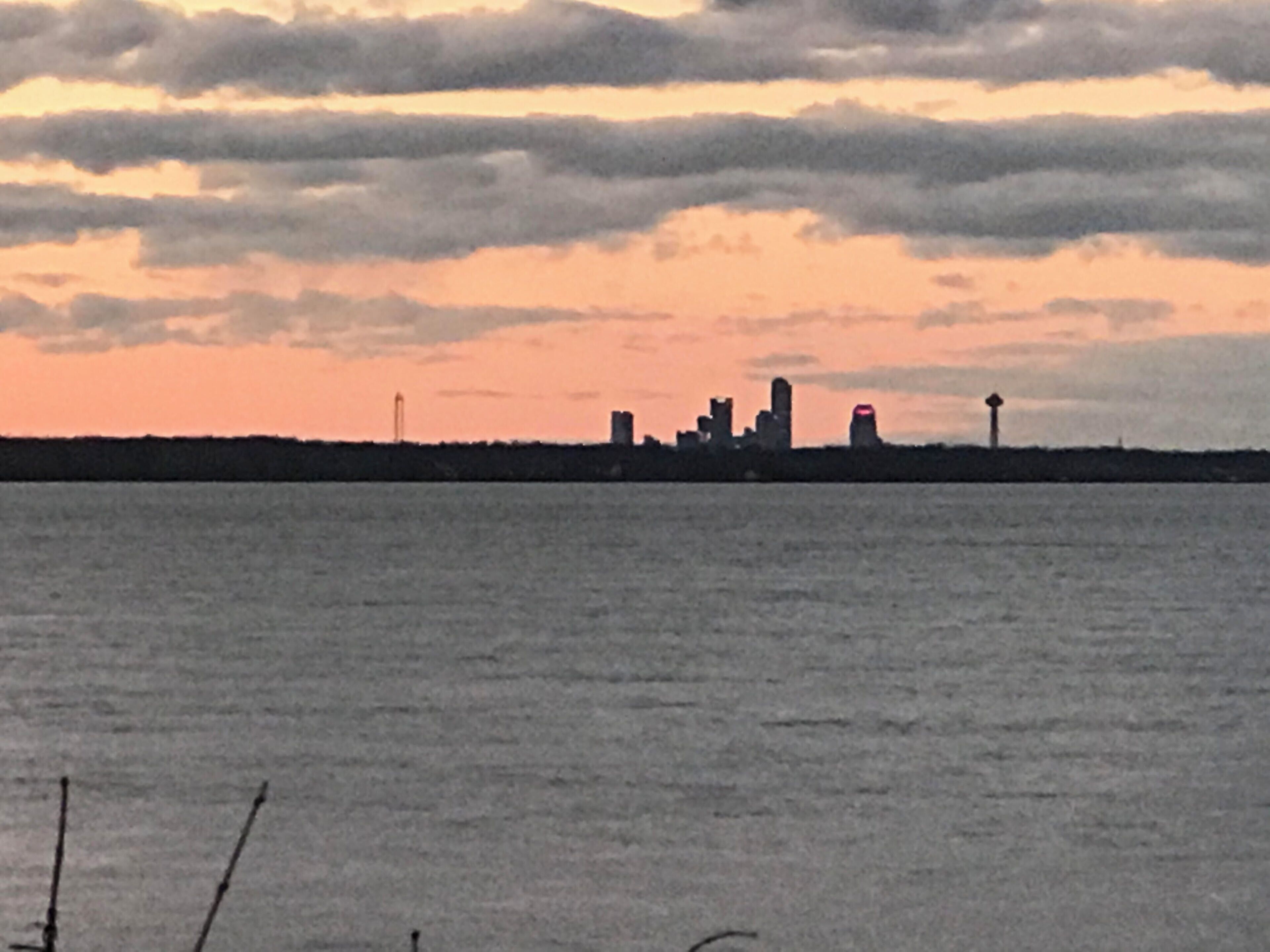 A city skyline silhouette against a sunset sky over a body of water.