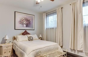 Une chambre Ă coucher bien rangĂ©e, avec un lit, des tables de chevet, une Ćuvre dâart accrochĂ©e au mur et une fenĂȘtre avec des rideaux.