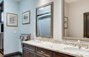 Une salle de bain avec un meuble-lavabo double, deux tableaux encadrés au mur et un grand miroir au-dessus du lavabo.