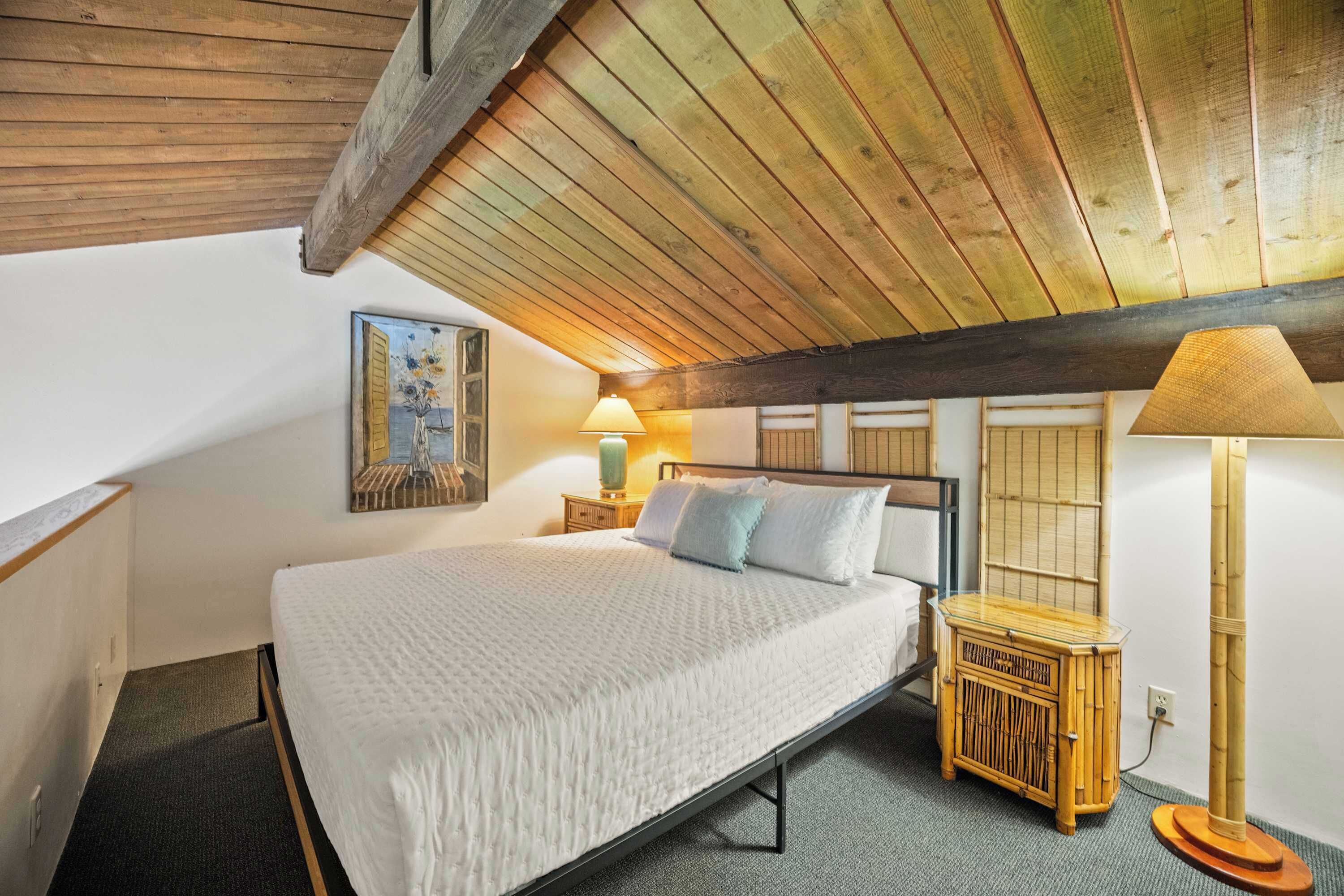 Ein Schlafzimmer mit Holzbalkendecke, einem Bett mit weißer Bettwäsche, einem Nachttisch mit Lampe und einem kleinen Holzschrank.