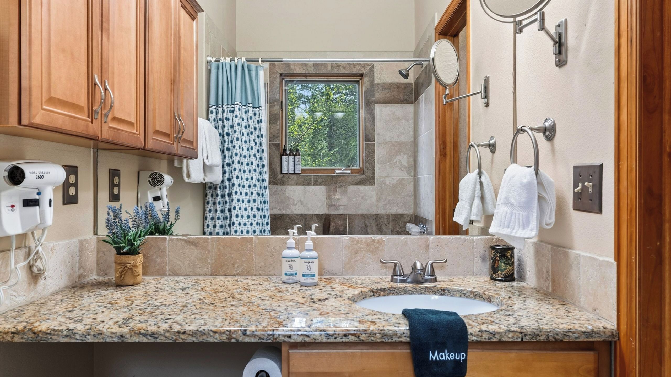 A bathroom with a granite countertop, a sink, a mirror, a towel rack, and a window with a view of trees.
