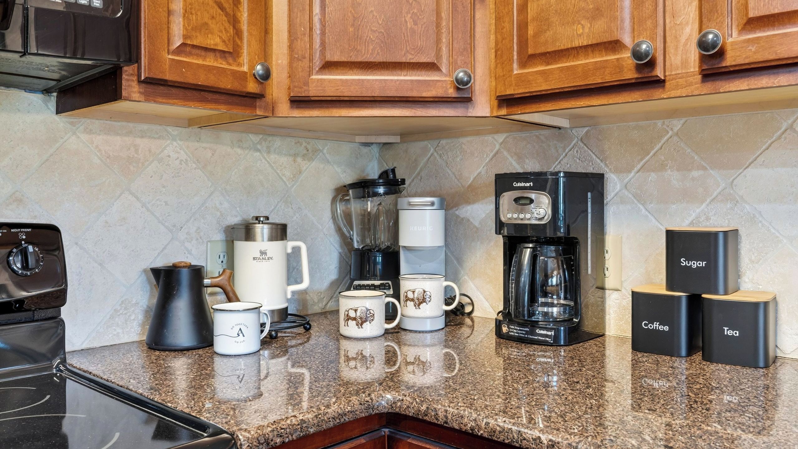 A kitchen with a coffee maker, a blender, a kettle, and coffee and tea containers.