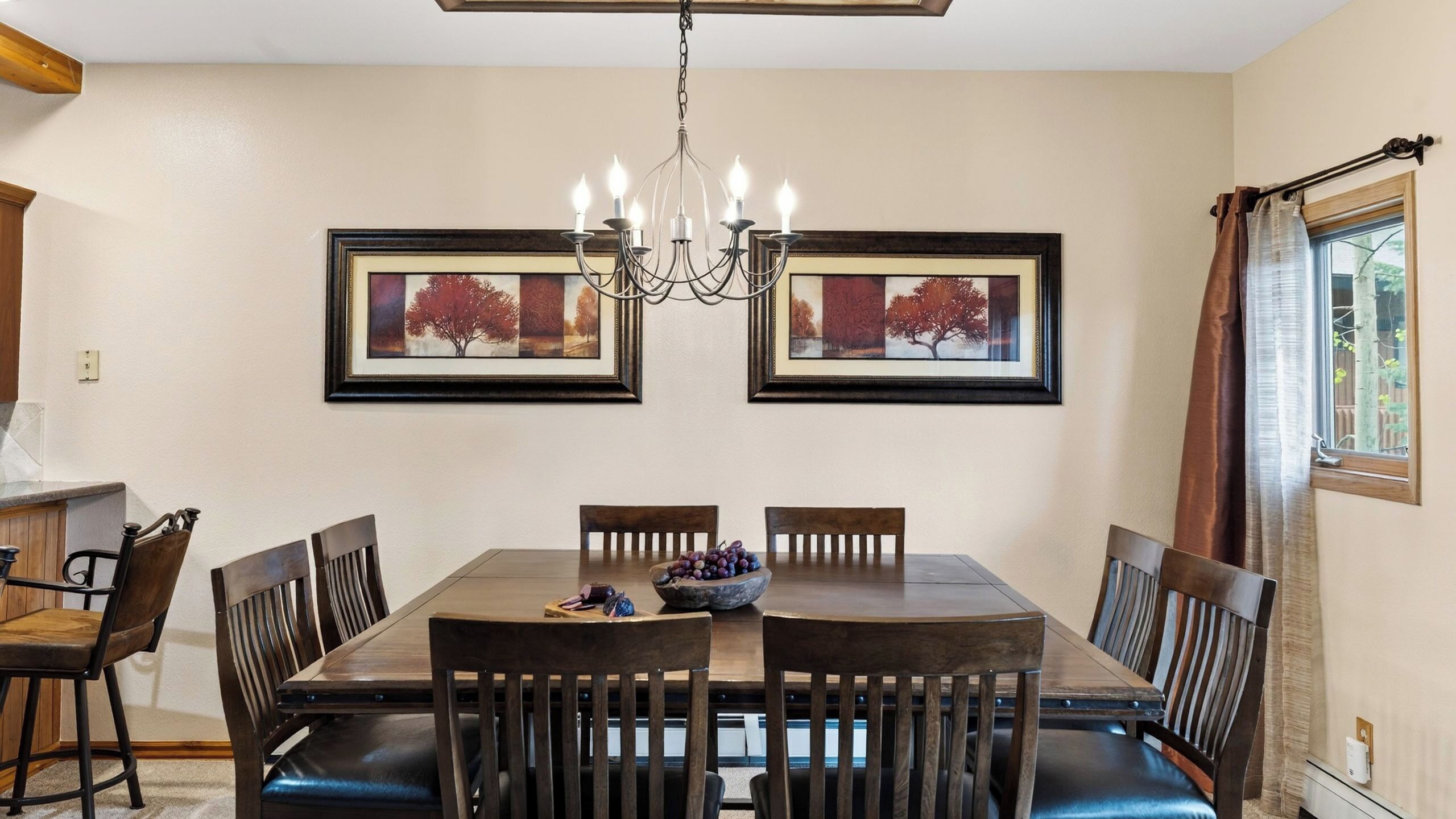Une salle à manger avec une table en bois, six chaises, un lustre et deux tableaux encadrés accrochés au mur.