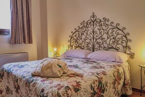 Una cama con colcha estampada, cabecero metálico decorativo y lámpara de noche.