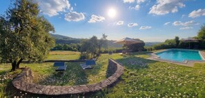 Zona de piscina con un sendero de piedra, sillones de descanso y una pérgola con sombrilla.