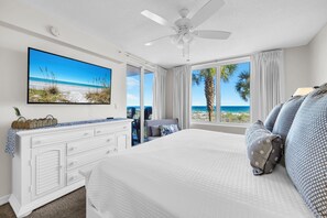 Ein Schlafzimmer mit Bett, Fernseher, Deckenventilator, Kommode und einem großen Fenster mit Meerblick.