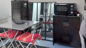 A compact kitchen with a microwave, a red clock, and a small dining area with a table and chairs. - Apartment in Cap Ferret, across from Phare Beach (Lège-Cap-Ferret)
