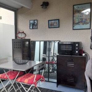 A compact kitchen with a microwave, a red clock, and a small dining area with a table and chairs. - Apartment in Cap Ferret, across from Phare Beach (Lège-Cap-Ferret)