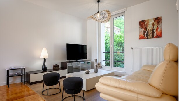 Een moderne woonkamer met een bank, televisie, lamp en kunstwerk.