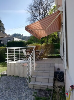 Un espace extérieur abrité, doté d’une rambarde en métal, d’une petite table et de chaises, ainsi que d’un escalier menant à un niveau supérieur.