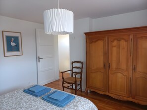 Une pièce comprenant un lit, une armoire en bois, une chaise et un luminaire suspendu.