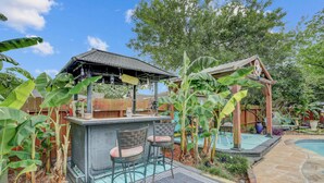 Un jardin avec un espace bar, une piscine et une structure en bois.