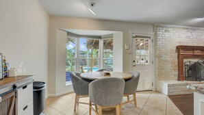 Une cuisine avec une table ronde, des chaises grises, une poubelle et une vue sur l’extérieur.