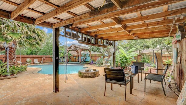 Un patio couvert avec une piscine, des sièges d’extérieur et une pergola en bois.