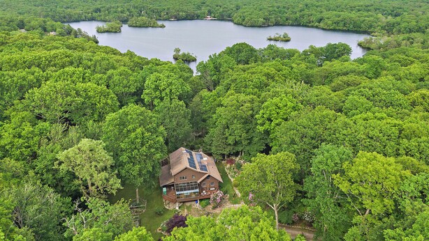 A house surrounded by dense forest with a lake in the background.