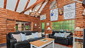 A log cabin interior with a wooden ceiling, two leather sofas, a wooden coffee table, and a television.