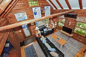 Ein Innenraum einer Blockhütte mit Wohnbereich, Holzwänden, Kamin und Fernseher.