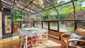 A conservatory with a table and chairs, large windows, and a view of the outdoors.