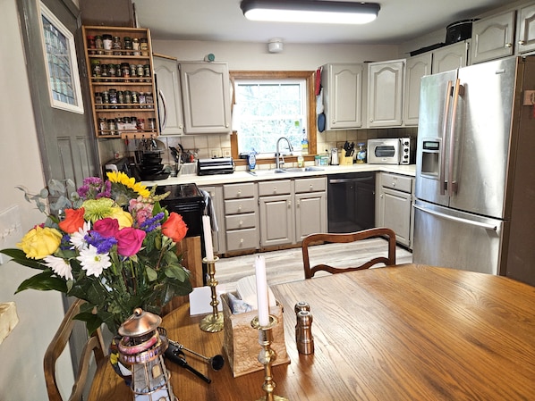 A kitchen with wooden cabinets, a stainless steel refrigerator, a microwave, and a dining table with a vase of flowers.