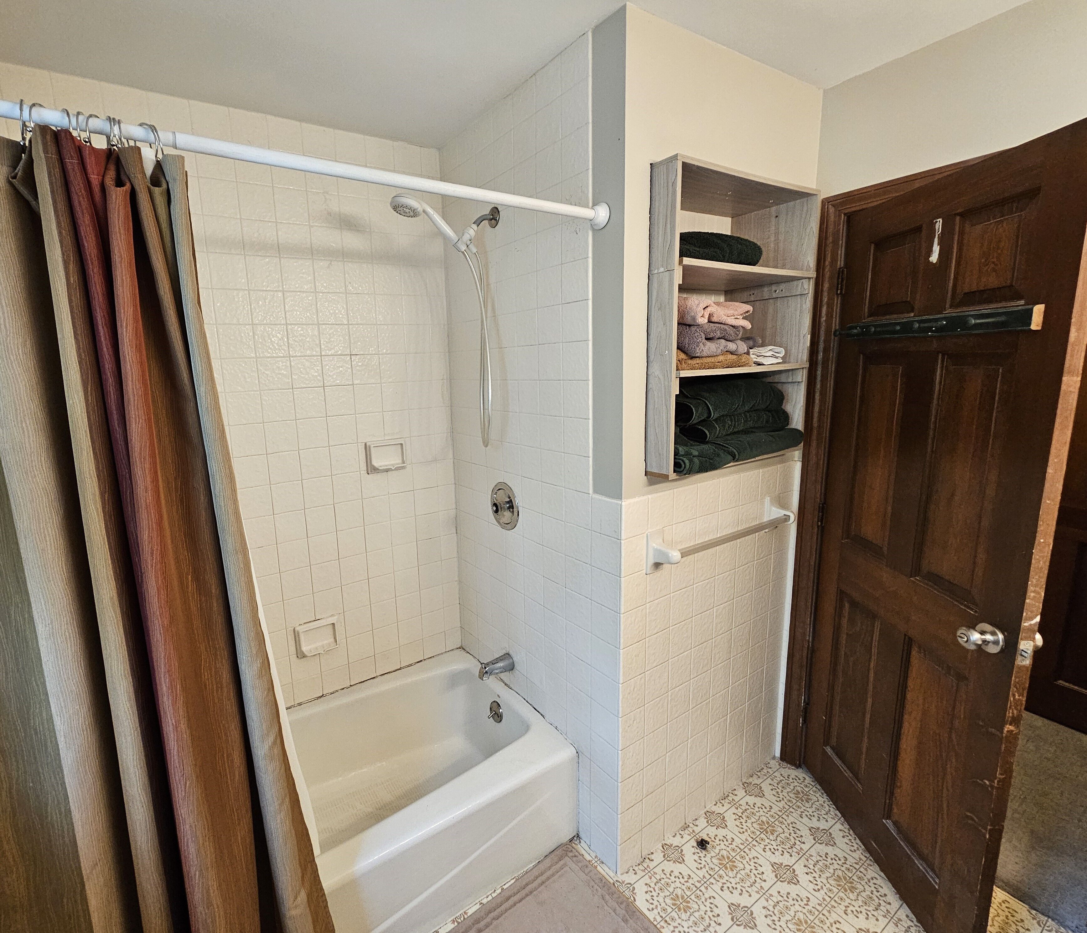 A bathroom with a bathtub, shower, and a wooden door.