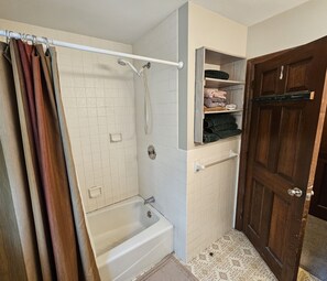 A bathroom with a bathtub, shower, and a wooden door.