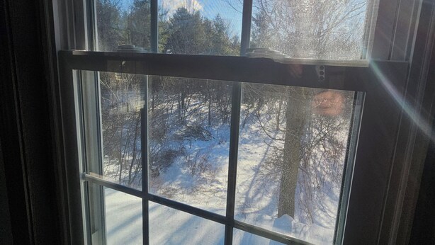 Ett fönster med utsikt över ett snötäckt landskap och kala träd.