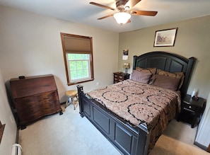 A bedroom with a bed, dresser, nightstand, lamp, and a ceiling fan.