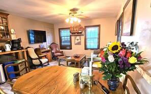 A dining area with a wooden table, chairs, a ceiling fan, and a vase of flowers.