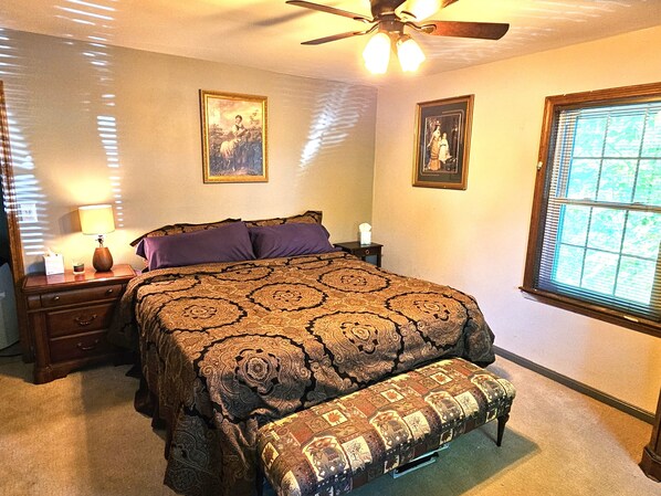 A bedroom with a bed, a nightstand, a lamp, a ceiling fan, and two framed pictures on the wall.