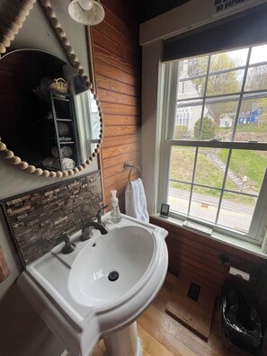 A bathroom with a white sink, wooden paneling, a mirror with a bead trim, and a view of a house through a window.