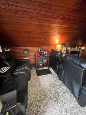 A cozy room with wooden walls, a fireplace, a coffee station, and leather seating.