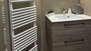 A bathroom with a white towel rack, a sink with a mirror, and a wooden vanity. - Charming villa between sea and countryside in absolute calm (La Crau)