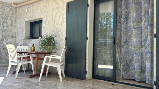 A room with a wooden table, two white chairs, a potted plant, a dark door, and a glass door with a leaf pattern. - Charming villa between sea and countryside in absolute calm (La Crau)