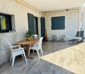 Una habitación con una mesa de madera, sillas blancas, una planta en maceta y un jarrón grande.