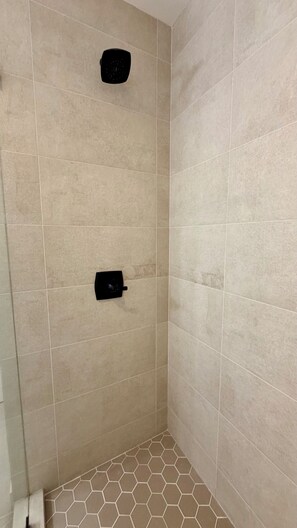 Un área de ducha con azulejos color beige y piso con patrón hexagonal.